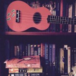 two shelves of books, a ukulele on the top shelf.